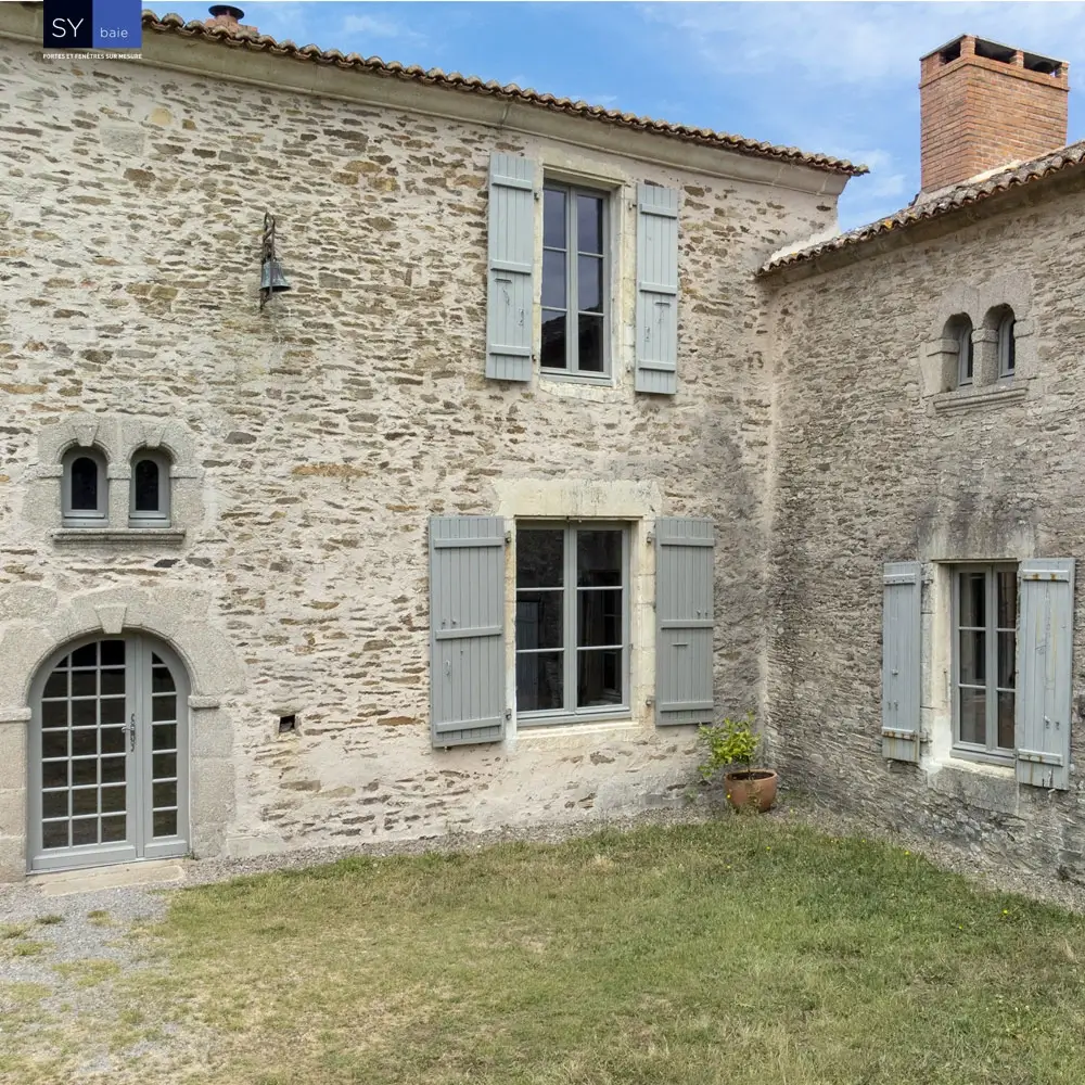 Façade maison pierre avec fenêtres blanches et volets bleus